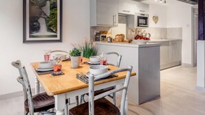 Une cuisine moderne dotée d’un îlot central, de meubles blancs et d’un coin repas avec une table et des chaises en bois.