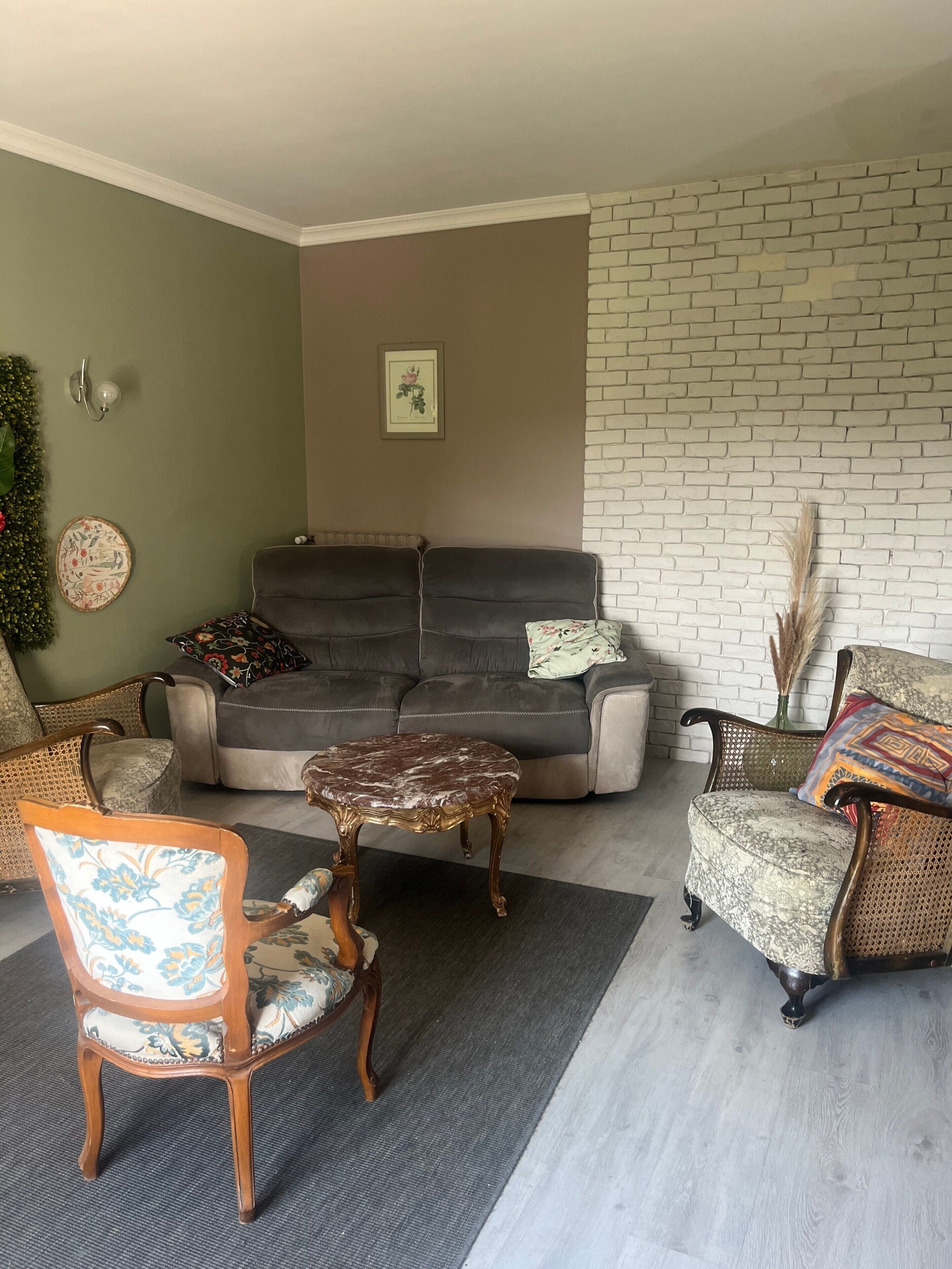 Un salon avec un canapé, deux fauteuils, une table basse et un mur en briques.
