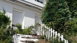 A white building with a white fence, stone steps, and greenery.