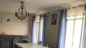 A dining area with a table, chairs, a chandelier, curtains, and a wall with a framed picture.