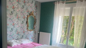 A bedroom with a bed, floral wallpaper, a mirror, a radiator, and a window with curtains.