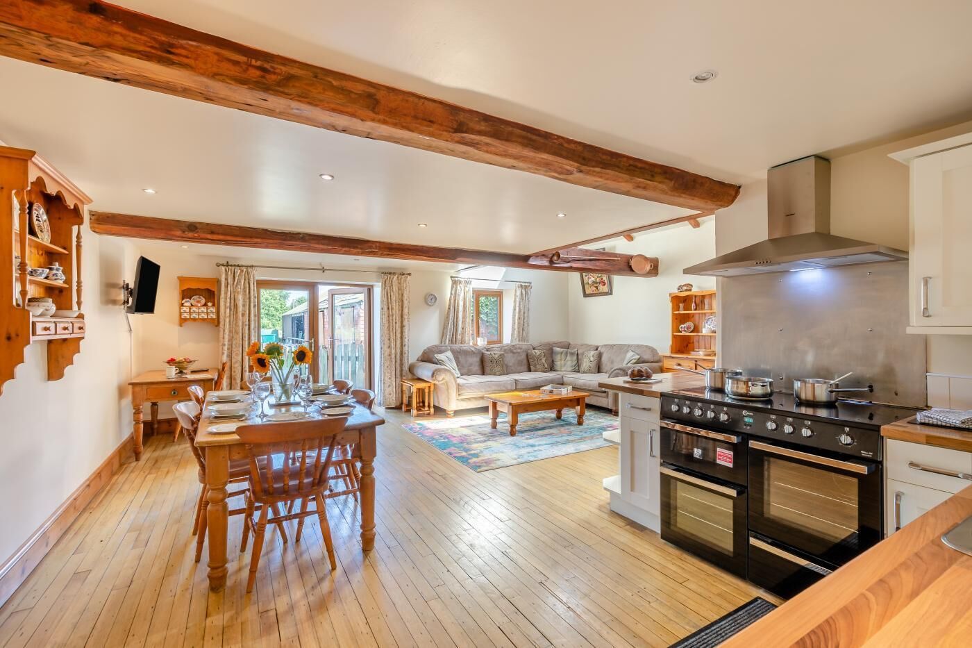 A spacious living area with a wooden dining table, a sofa, and a kitchen with modern appliances.