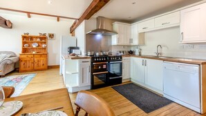 Una cocina compacta con armarios blancos, horno empotrado, lavavajillas y una mesa de comedor de madera con sillas.