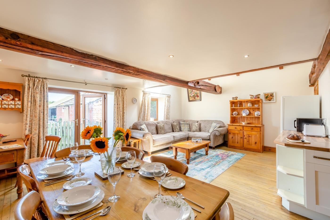 Ein Essbereich mit Holztisch, gedeckt für eine Mahlzeit, einer Couch und einer Küchenzeile mit Schränken und einem Kühlschrank.
