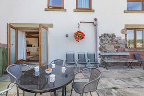 Eine Terrasse im Freien mit einem runden Tisch, Stühlen und einem hängenden Blumenkorb.