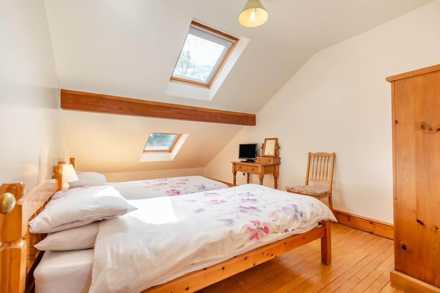 Ein Schlafzimmer mit schrägverdeckter Decke, zwei Betten, einem Schreibtisch, einem Stuhl und einem Kleiderschrank.