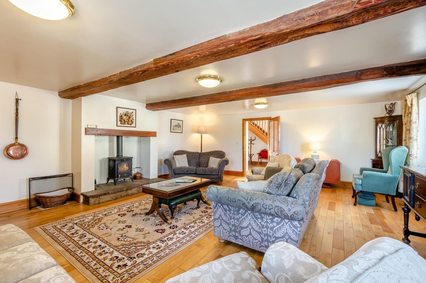 A cozy living room with a fireplace, sofas, a patterned rug, and wooden beams on the ceiling.