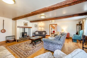 A cozy living room with a fireplace, sofas, a patterned rug, and wooden beams on the ceiling. - 5 Bed in Preston (oc-40993) (Pilling)
