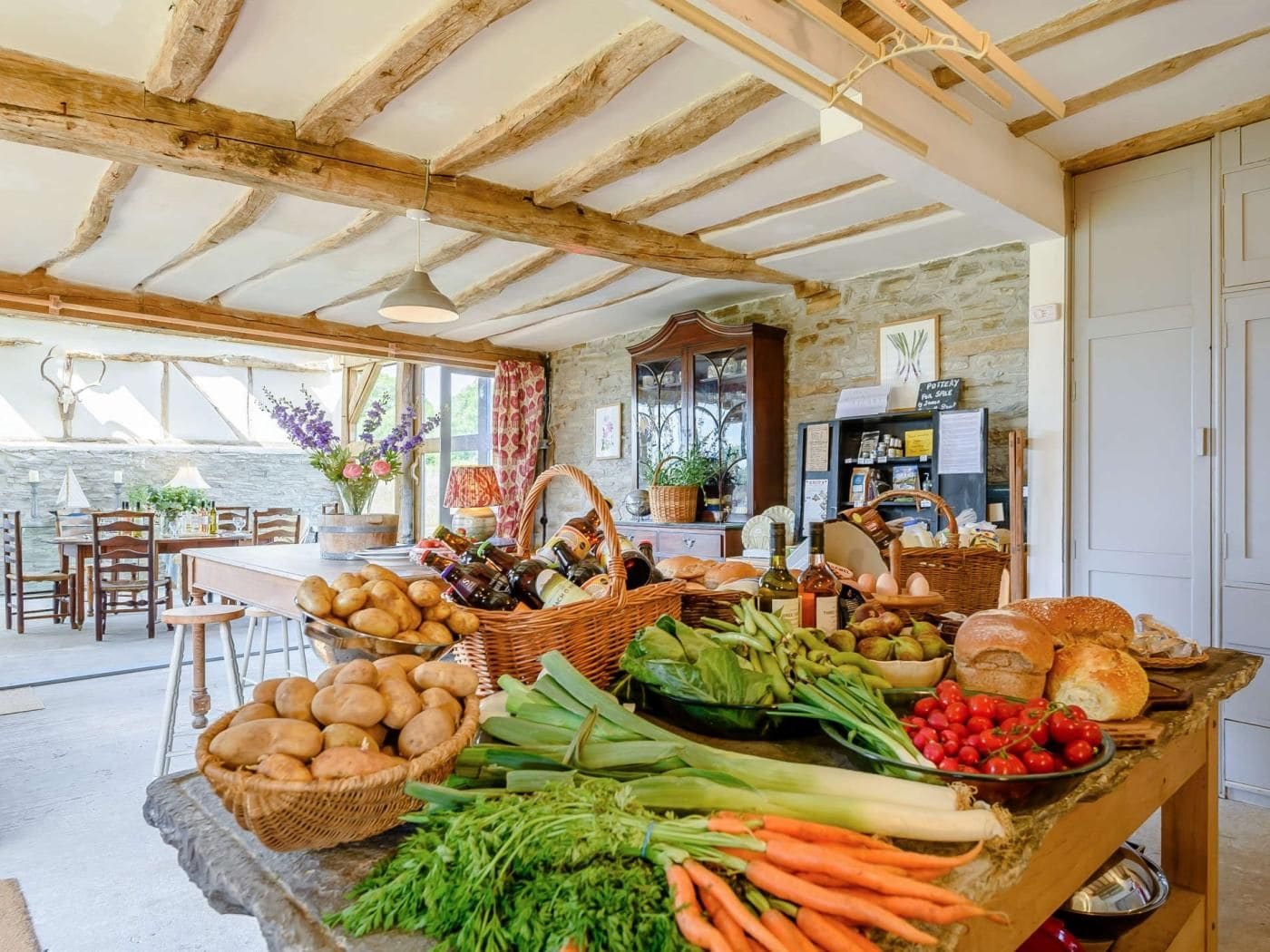 Une cuisine rustique avec un mur en pierre, des poutres en bois et une variété de produits frais et de pains disposés sur le comptoir.