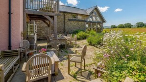 A stone building with a balcony, outdoor seating, and a garden with flowers.