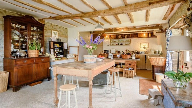 A rustic kitchen with wooden beams, a central island with stools, and a vintage cabinet.