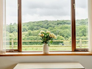 Ein Fenster mit Blick auf eine grüne Landschaft und eine weiße Vase mit Blumen auf einem Fensterbrett.