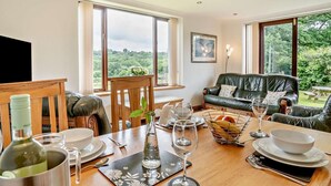 Un coin repas avec une table dressée pour quatre personnes, un canapé et une vue sur la verdure à l’extérieur.