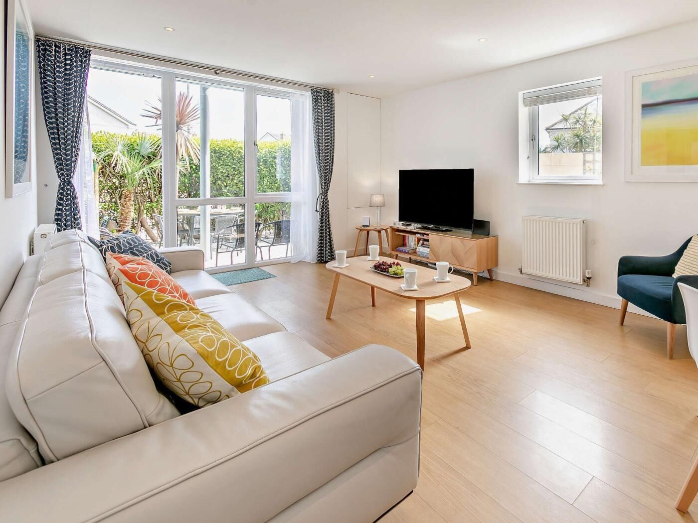 A modern living room with a sofa, coffee table, TV, and a view of greenery outside.