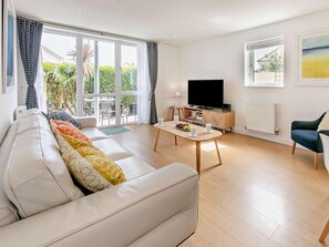 Ein modernes Wohnzimmer mit einer Couch, einem Couchtisch, einem Fernseher und Blick ins Grüne.