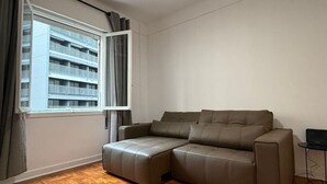 Ein modernes Wohnzimmer mit einem Ecksofa, einem kleinen Tisch und einem Fenster mit Vorhängen.