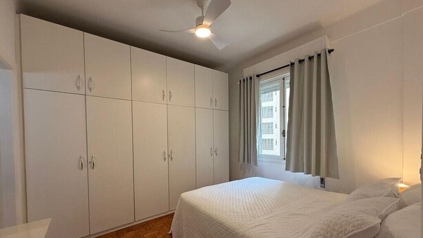 Ein Schlafzimmer mit Bett, weißem Kleiderschrank, Deckenventilator, Fenster mit Vorhängen und Holzboden.
