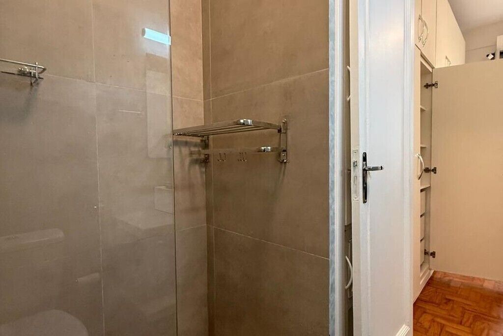 Un baño con cabina de ducha de vidrio, un perchero y una puerta blanca que da a un armario.