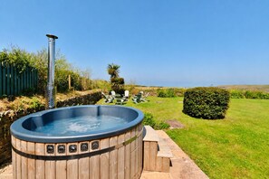 Ein Whirlpool in einem Garten mit einer Holzterrasse, Stühlen und Blick auf das Meer.