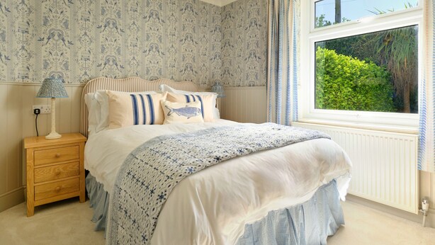 Een slaapkamer met een bed, nachtkastje, lamp en een raam met gordijnen.