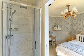 Ein Badezimmer mit Duschkabine und ein Schlafzimmer mit Bett, Schreibtisch und Nachttisch.