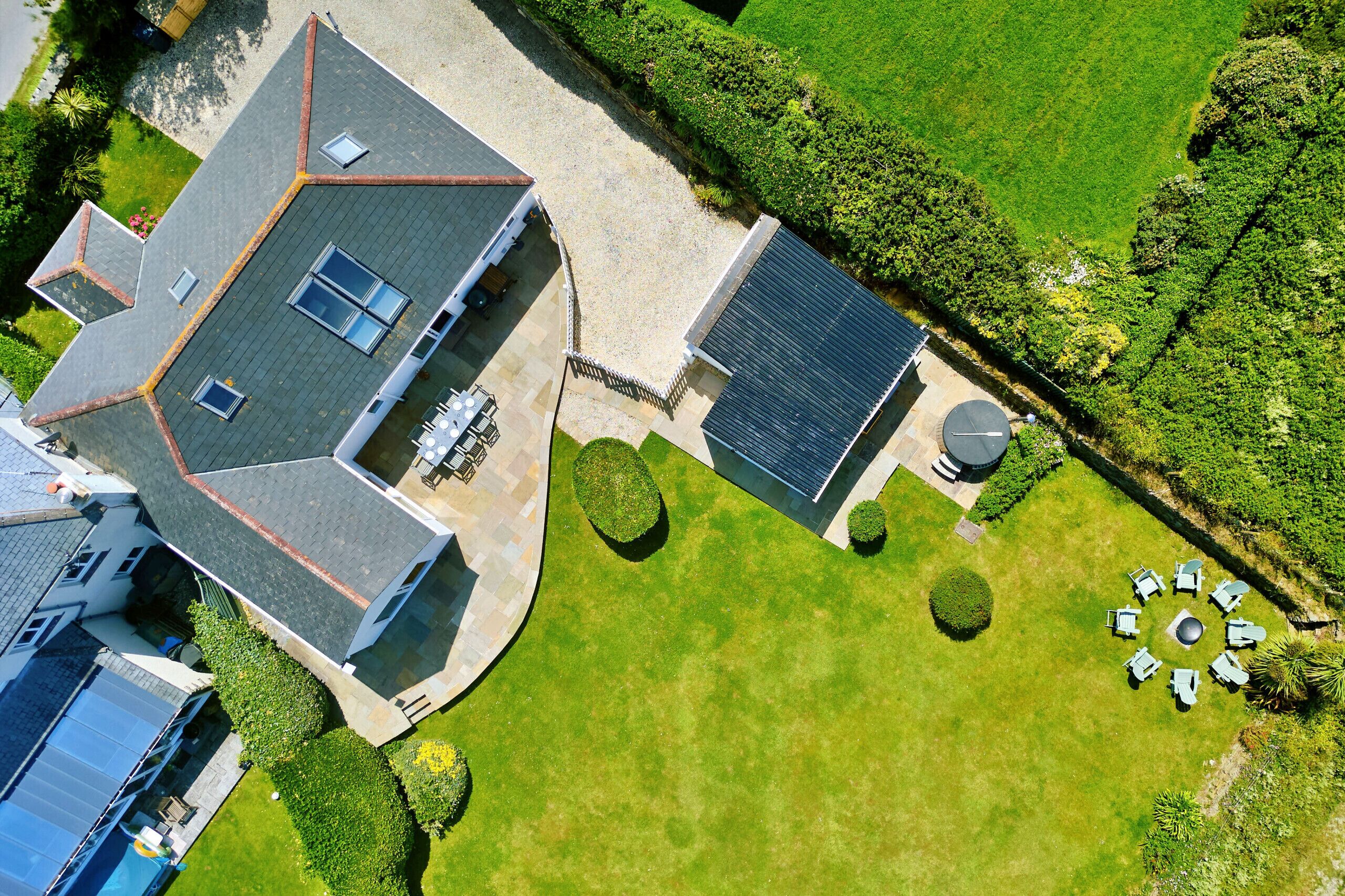 Vista aérea de una casa con entrada pavimentada, calentador solar de agua, una zona de estar circular y un césped bien cuidado.