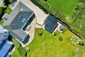 An aerial view of a house with a paved driveway, a solar water heater, a circular seating area, and a well-maintained lawn. - The Coast House (Porthcothan Bay)