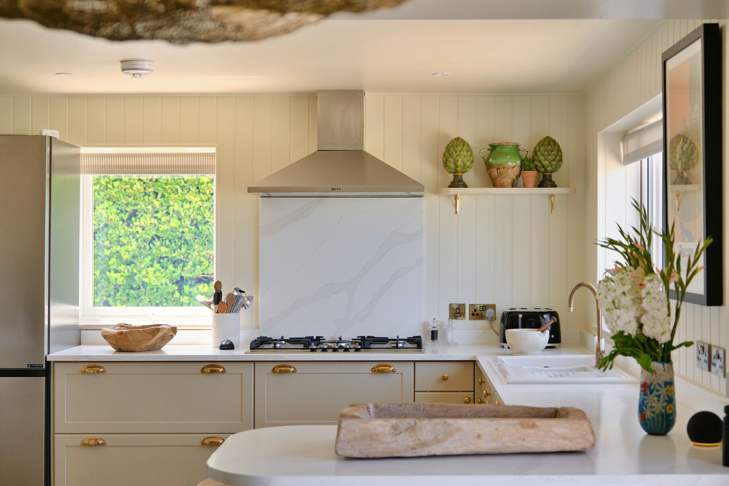 A modern kitchen with a gas stove, white cabinets, a window with a view, and a decorative vase.