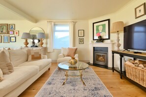 A living room with a sofa, a glass coffee table, a fireplace, and a television. - The Coast House (Porthcothan Bay)
