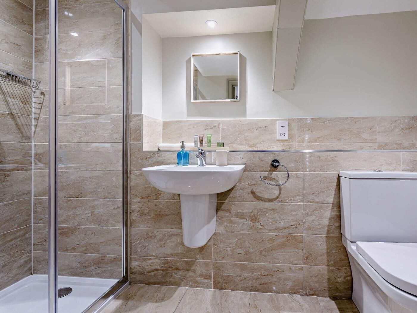 Une salle de bain avec une douche à parois de verre, un lavabo blanc avec un miroir au-dessus et des toilettes.
