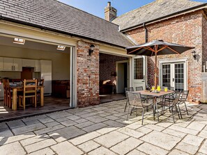 Une terrasse avec une table et des chaises, un mur en briques et une porte donnant sur un garage.