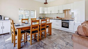 A modern kitchen with white cabinets, a dining table with chairs, and a stone-tiled floor. - 3 Bed in Taunton (oc-blaba) (Hillcommon)