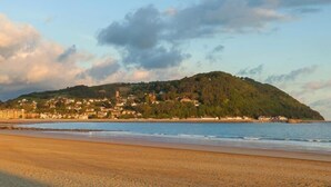 A coastal town with buildings on a hill, a beach, and a clear sky. - 3 Bed in Taunton (oc-blaba) (Hillcommon)