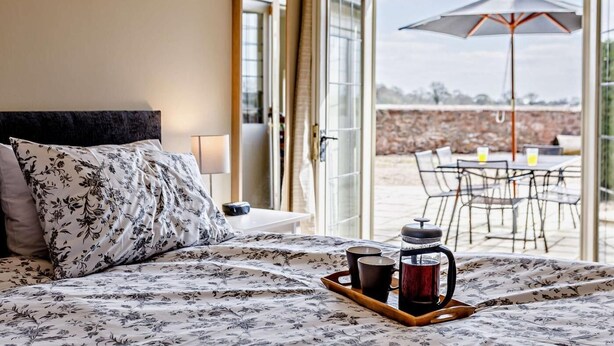 A hotel room with a bed, a tray with a coffee pot and cups, and an outdoor patio with chairs and an umbrella. - 3 Bed in Taunton (oc-blaba) (Hillcommon)