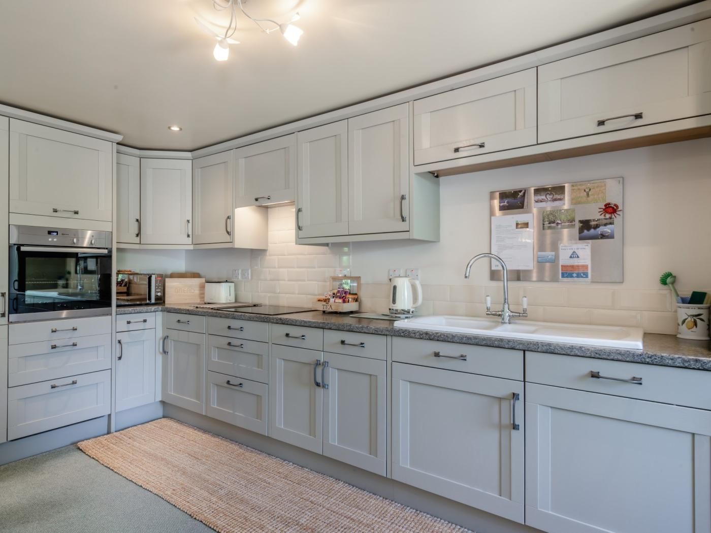 A modern kitchen with white cabinetry, a built-in oven, a sink, and a countertop with various appliances.