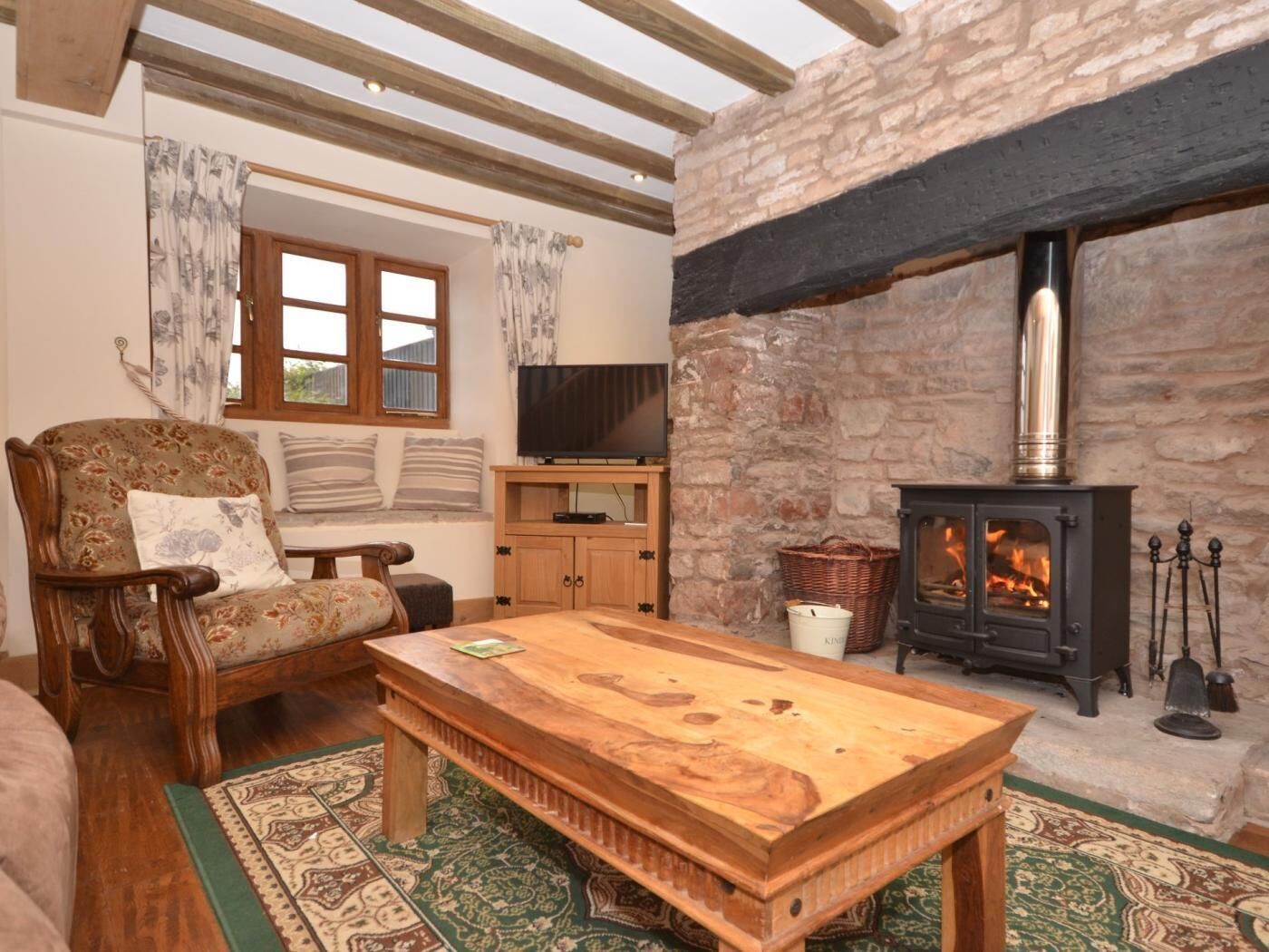 A cozy living room with a stone fireplace, wooden furniture, and a television.