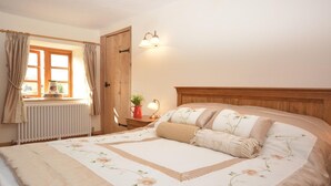 Una camera da letto con un letto, una finestra con tende, un termosifone, un comodino con una lampada e una porta in legno.