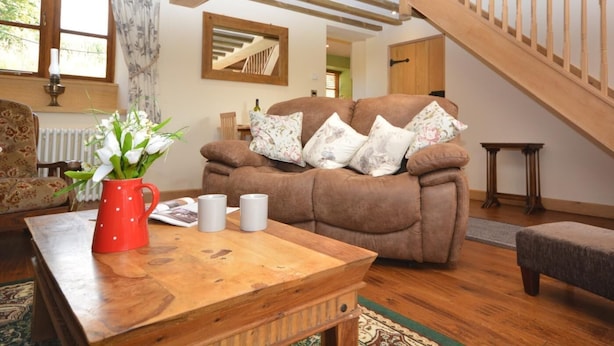Un accogliente soggiorno con soffitto in legno, un divano marrone con cuscini a motivi floreali, un vaso rosso con fiori e un tavolino da caffè in legno.