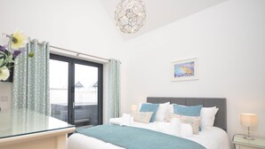 A bedroom with a bed, bedside tables, a window with curtains, a wall-mounted light fixture, and a painting. - 3 Bed in Bideford (oc-40820) (Northam)