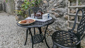 A table with a teapot, cups, and cookies, set against a stone wall with a lattice and flowering plants. - 3 Bed in Redruth (oc-37014) (Saint Day)