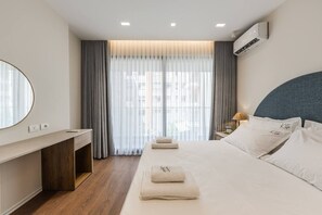 A hotel room with a bed, bedside table, lamp, air conditioning unit, and a large window with curtains. - Kiti Apartment | Beach Escape by PikHost (Vlorë)