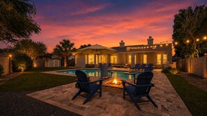 Un patio trasero con piscina, mobiliario exterior y una chimenea.