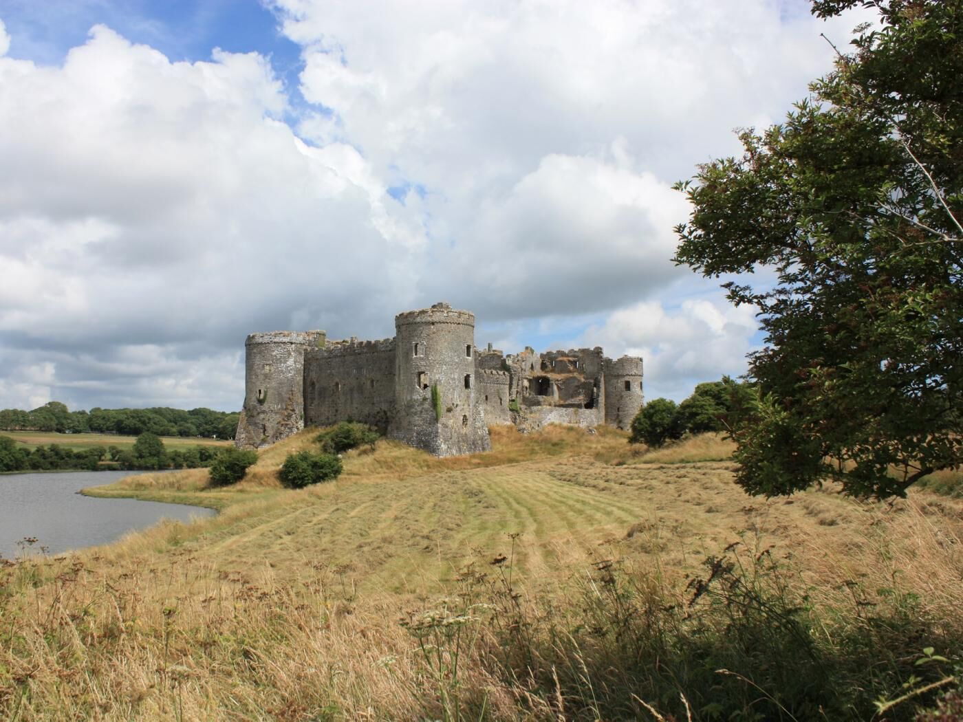 A historic castle with multiple towers, surrounded by a grassy landscape and a body of water.