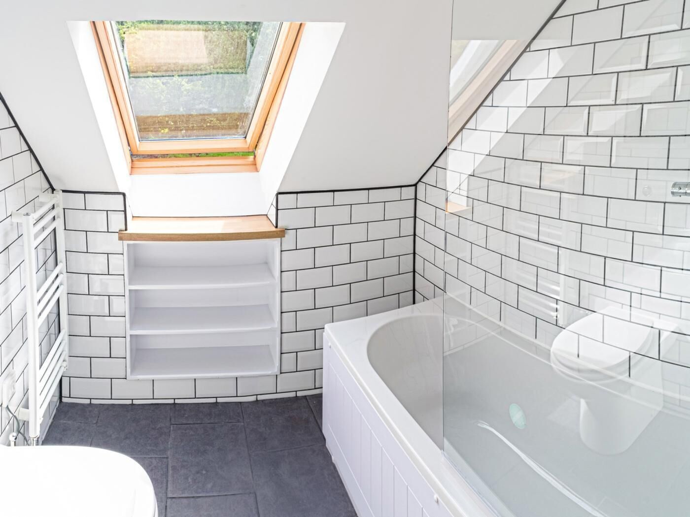 A modern bathroom with a skylight, white tiled walls, a bathtub, and a shower area.