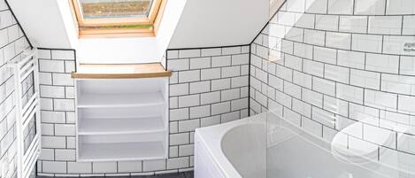 A modern bathroom with a skylight, white tiled walls, a bathtub, and a shower area.