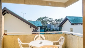 Un balcón con mesa y sillas, vista a edificios vecinos y cielo despejado.