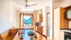 Un comedor con una mesa de madera, sillas, un ventilador de techo y una cocina con armarios y estufa.