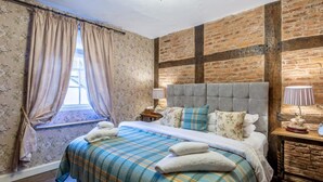 Un dormitorio con cama, cortinas, un candelabro, una pared de ladrillo y una mesita de noche.
