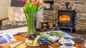 Una habitación acogedora con chimenea, una mesa servida con queso, uvas y galletas, y un jarrón de tulipanes.