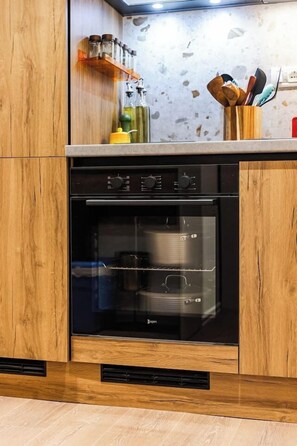 A kitchen with wooden cabinets, a built-in oven, a countertop with a knife block, and a spice rack. - Kiti Studio | Beach Escape by PikHost (Vlorë)